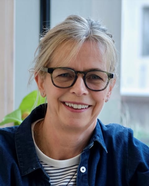 Anna Ford, KST therapist, smiling, in glasses and a denim shirt